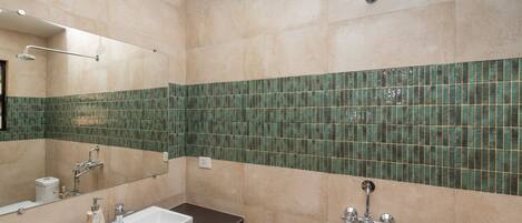 A bathroom with beige tiles, a green-tiled accent wall, a white sink, and a handheld showerhead.