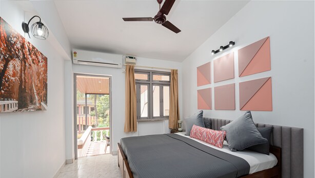 A bedroom with a bed, a ceiling fan, an air conditioning unit, a window with curtains, and a wall with geometric patterns. - Villa Calangute Phase 7 (Candolim)