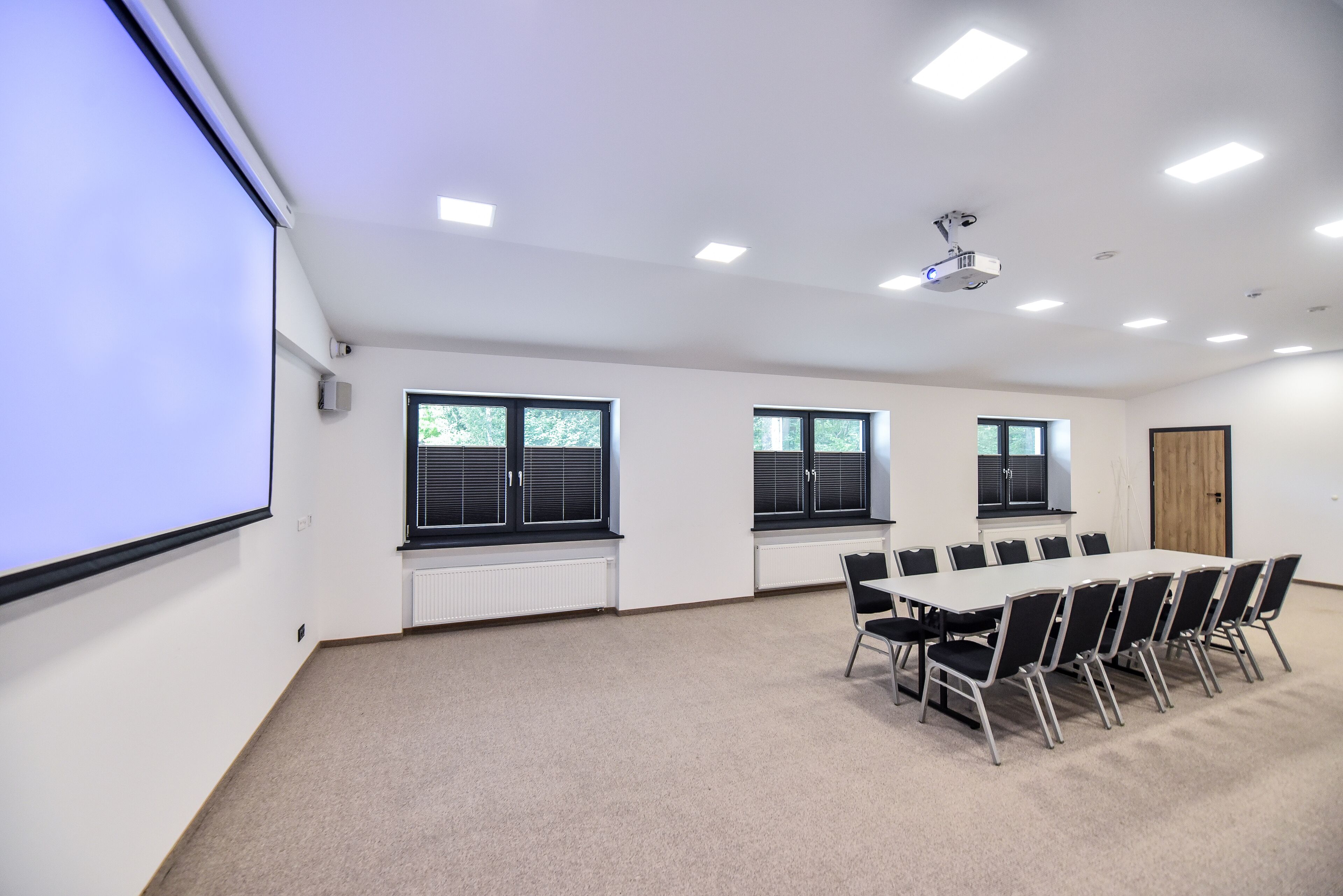 A conference room with a long table, chairs, a projector, and windows.