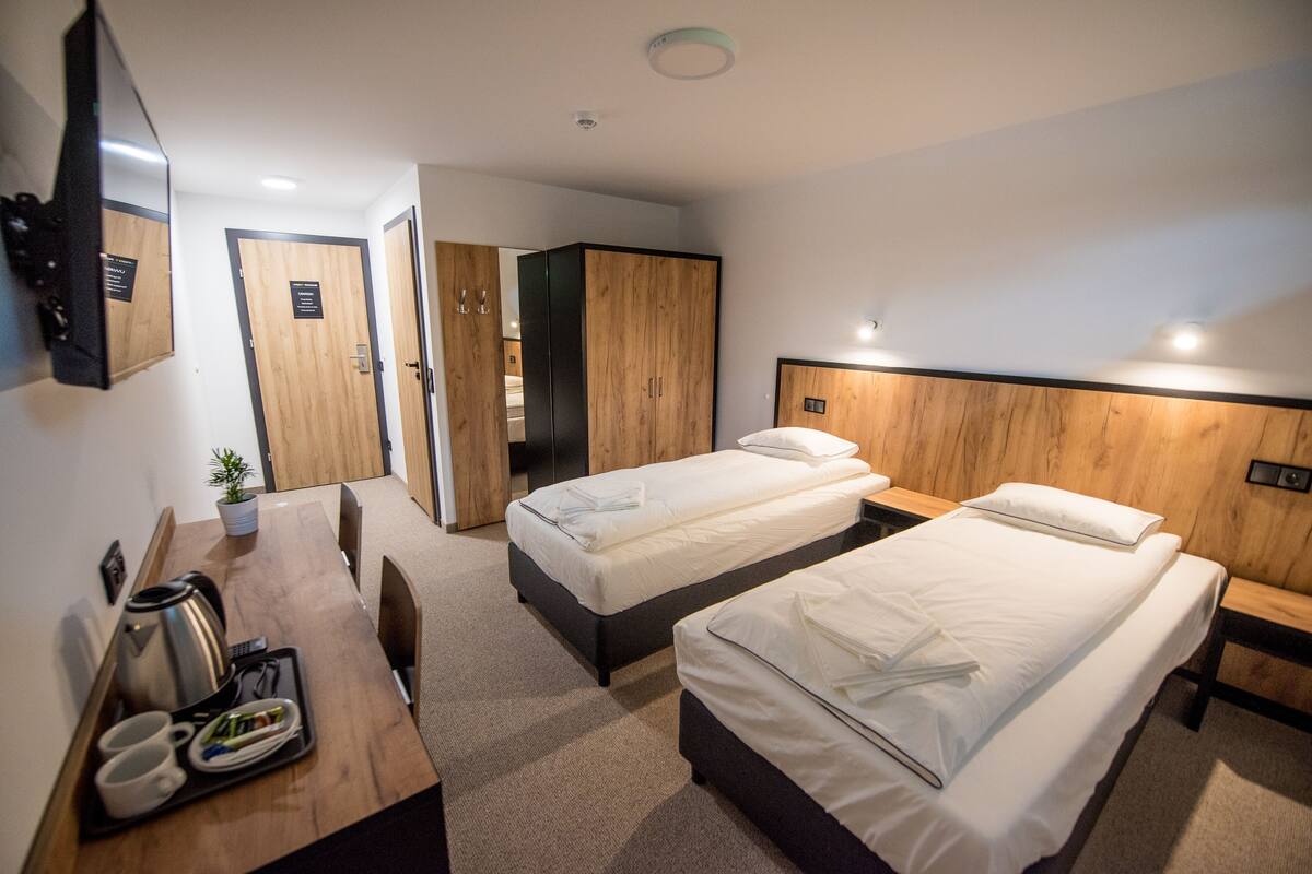 A hotel room with two beds, a desk with a kettle, cups, and a tray, and a mirror on the wall.