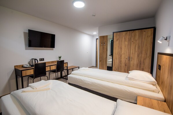A hotel room with two single beds, a desk with a chair, a TV mounted on the wall, and a wardrobe. - Sport Rooms Spała (Inowlodz)