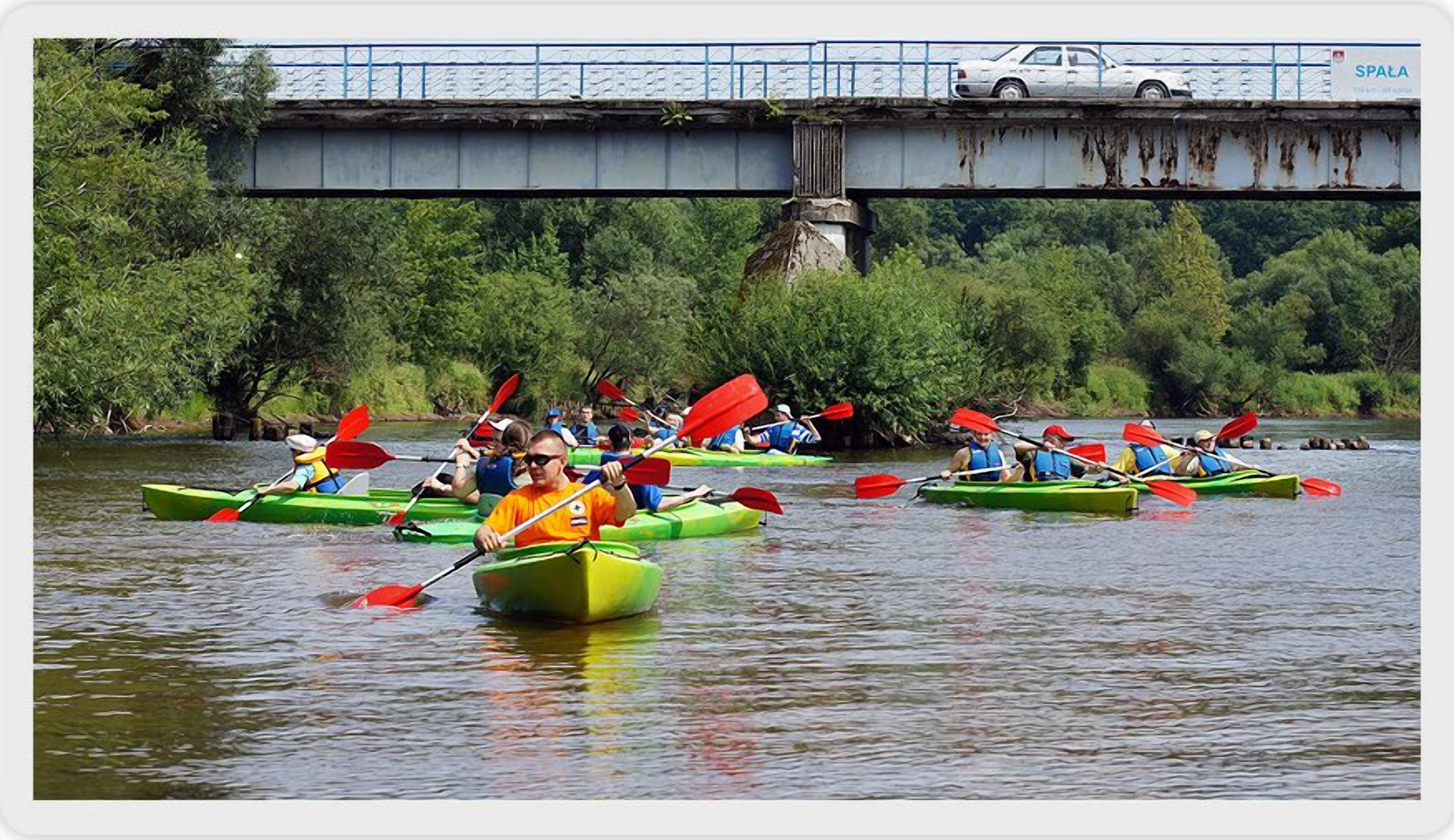 A group of people kayaking on a river under a bridge.