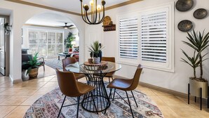 A dining area with a round glass table, four brown chairs, a chandelier, and a patterned rug. - Cozy Ranch-Style Condo - A Ryson Property (Palm Springs)