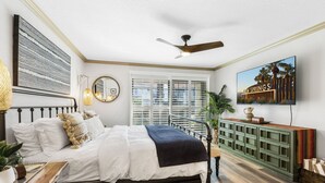 A bedroom with a bed, a ceiling fan, a TV, a window, and a green cabinet. - Cozy Ranch-Style Condo - A Ryson Property (Palm Springs)