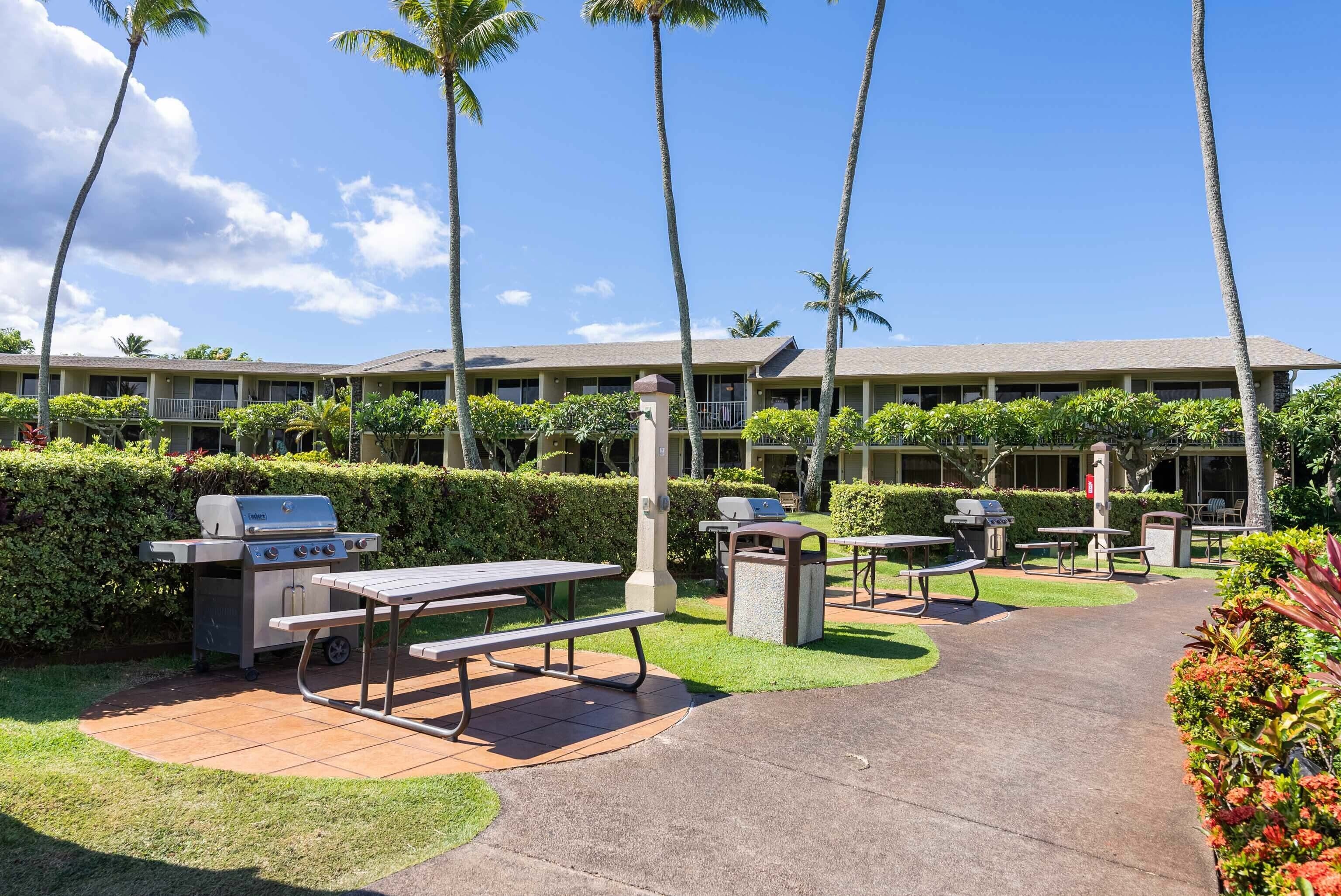 An outdoor patio area with grilling stations, picnic tables, and a building in the background.