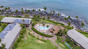 Oversigtsbillede af et resort med en swimmingpool, solpaneler på bygningerne og en strand med palmetræer.
