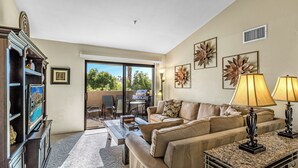 A living room with a sofa, coffee table, and entertainment unit. There is a sliding glass door leading to a patio area. - Classic Comfort in Central PS - A Ryson Property (Palm Springs)