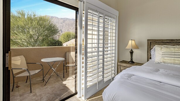 A hotel room with a bed, a small table, a chair, and a balcony with a view of the mountains. - Classic Comfort in Central PS - A Ryson Property (Palm Springs)