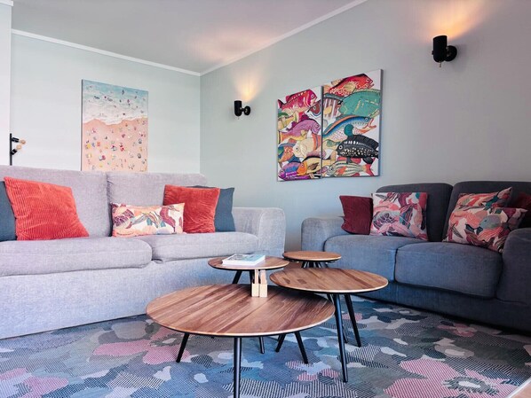 A modern living room with two grey sofas, colorful cushions, a patterned rug, and a wall with a large fish-themed artwork.