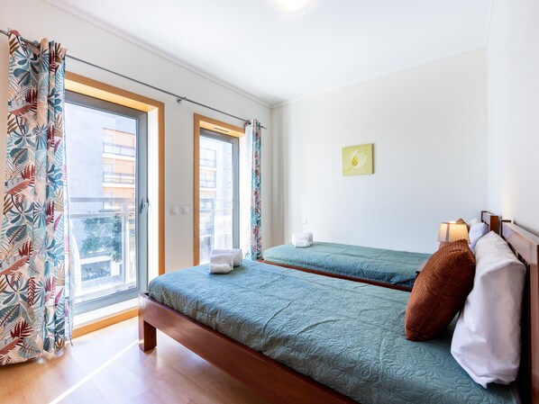 A hotel room with two beds, a balcony, and a view of buildings. - Apartment Baixa Marina (Olhão)