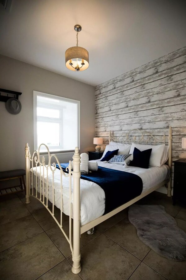 A bedroom with a white metal bed frame, a blue and white bedspread, a wooden wall, and a hanging light fixture.