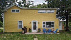 A yellow house with a front porch, two windows, and a door. There are two blue chairs and a table on the porch. - Restful Farm Retreat (Cincinnati)