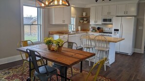 A modern kitchen with white cabinets, a wooden dining table, and a hanging light fixture. - Restful Farm Retreat (Cincinnati)