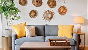 Ein Wohnzimmer mit grauem Sofa, gelben Kissen, einem Holztisch und einer Wand mit gewebten Wandbehängen.