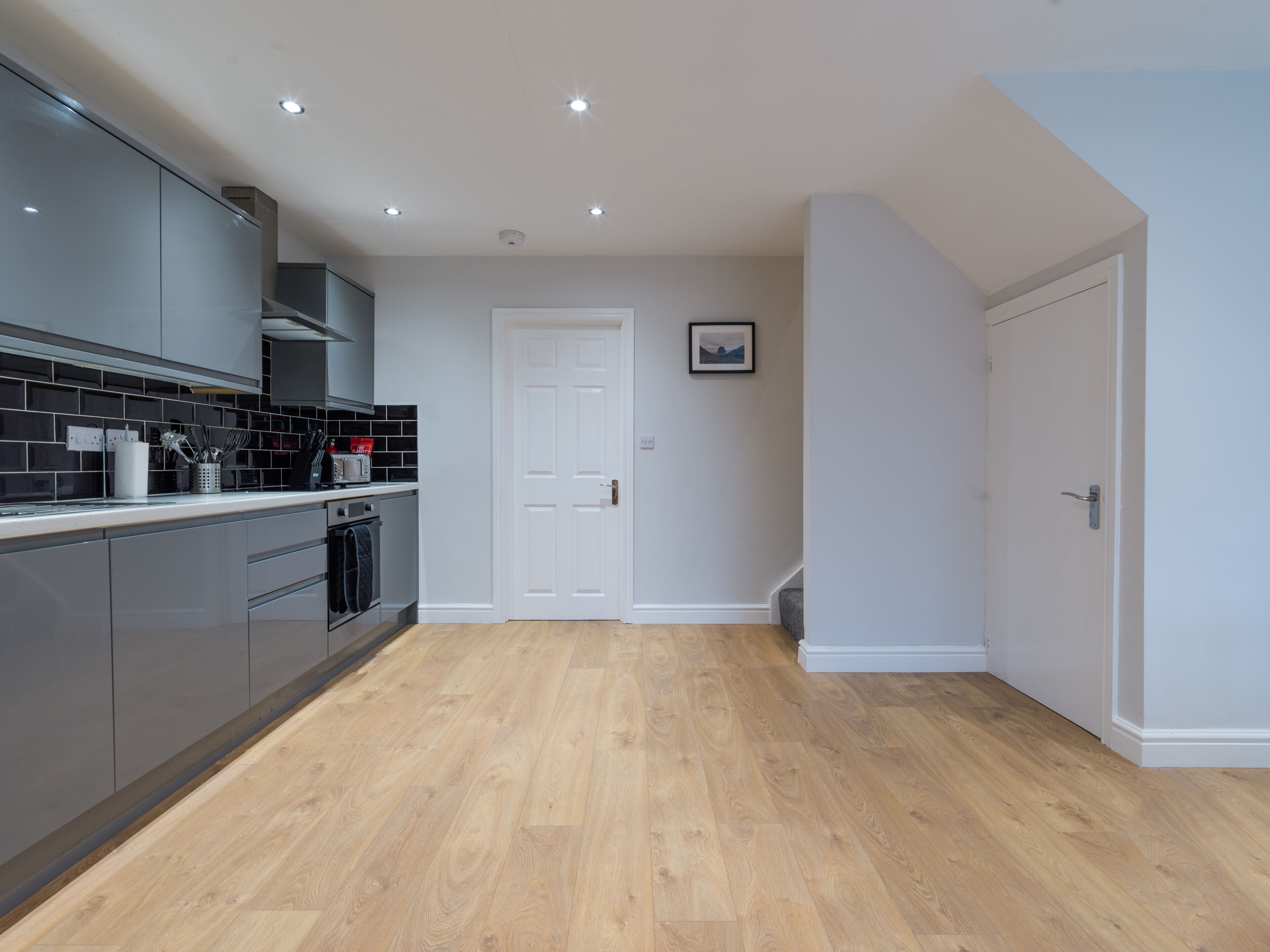 A modern kitchen with grey cabinets, a stainless steel range hood, and a wooden floor.