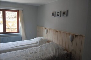 A bedroom with two beds, a window with curtains, and three wall-mounted pictures.