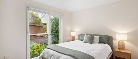 Quarto com uma cama grande, duas mesas de cabeceira com luminárias, uma janela com vista para um jardim e uma luminária no teto.