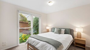 Un dormitorio con una cama grande, dos mesitas de noche con lámparas, una ventana con vistas a un jardín y una lámpara en el techo.