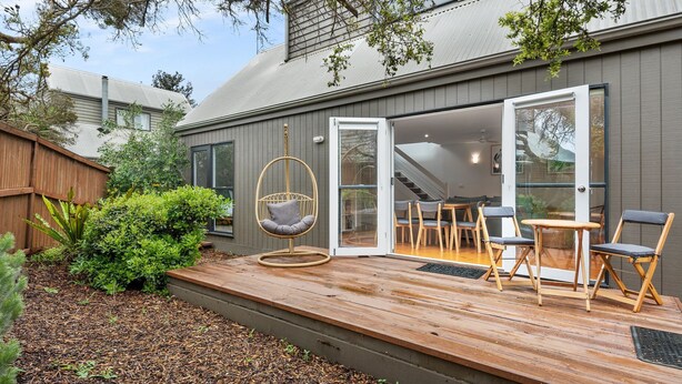 Une maison moderne dotée d’une terrasse en bois, d’un fauteuil suspendu et d’un coin repas avec des chaises et une table.