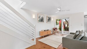 Un salon moderne avec un escalier, un canapé gris, un meuble en bois et un ventilateur de plafond.