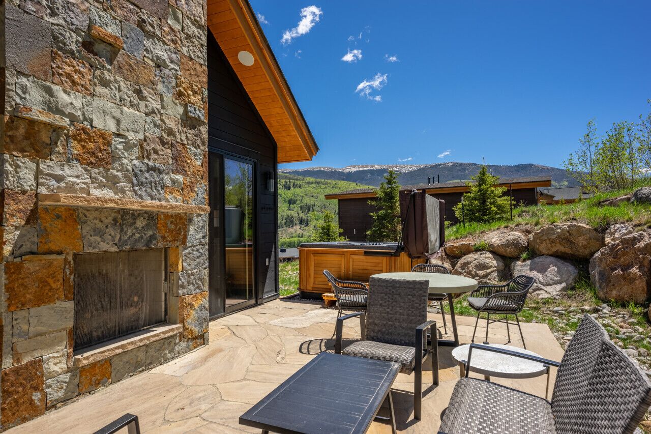 A stone exterior wall, a patio with outdoor furniture, and a view of mountains.