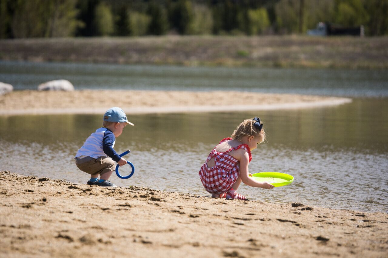 Dos niños jugando cerca de un lago con orilla de arena.