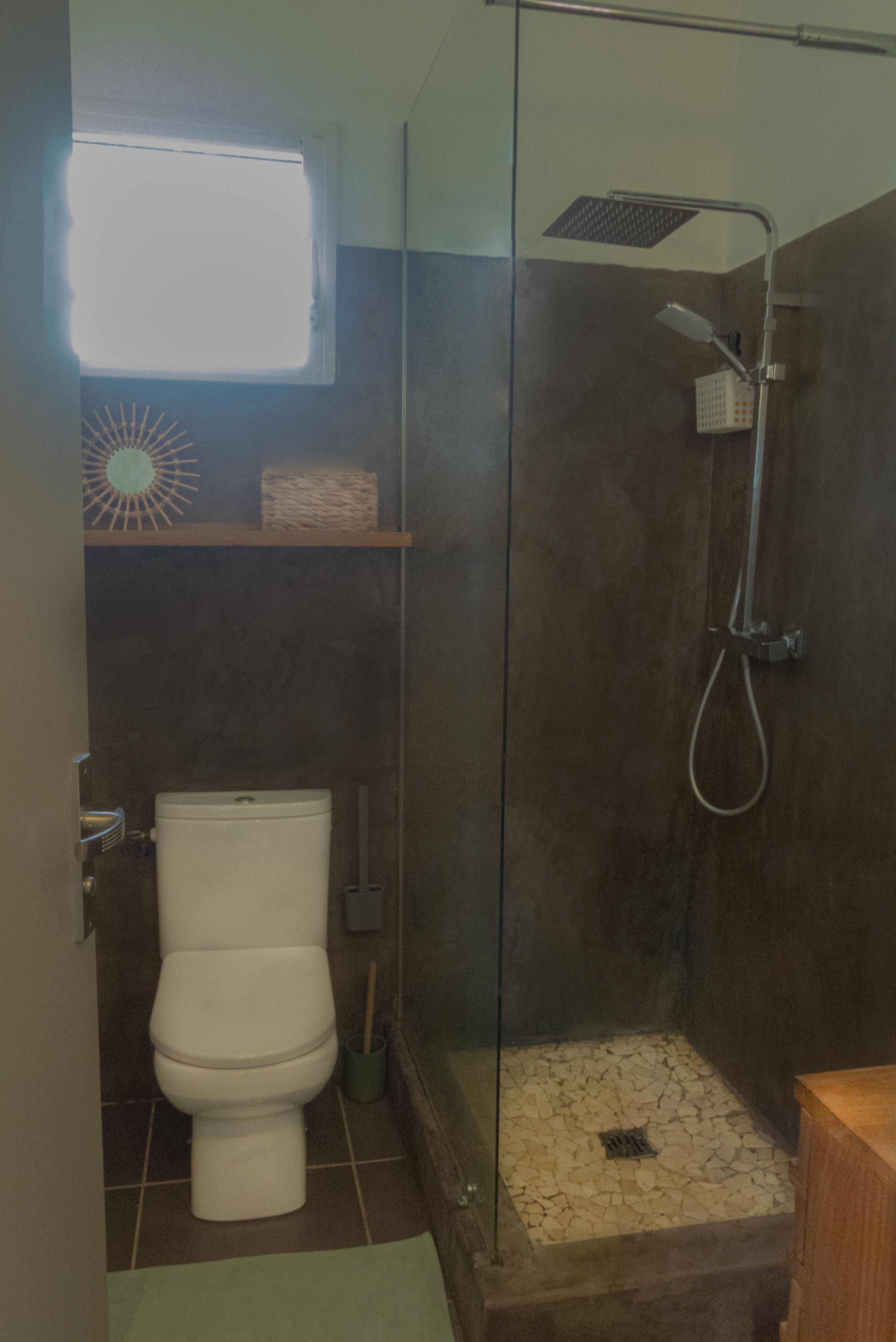 Ein Badezimmer mit einer Duschkabine, einer Toilette und einem Regal mit einem Korb.