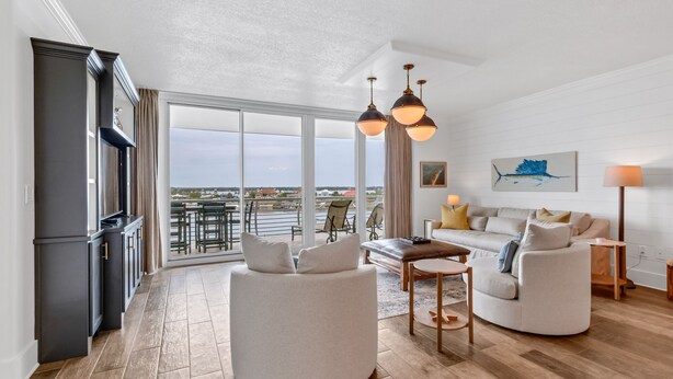A spacious living area with a large window offering a view of the water, a modern kitchen, and a seating area with a sofa and armchairs. - Bella Luna 504 by Liquid Life (Orange Beach)