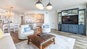 A modern living room with a large TV, a dining area, and a kitchen. - Bella Luna 504 by Liquid Life (Orange Beach)