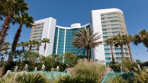 A modern hotel with a curved facade, multiple balconies, and lush tropical landscaping. - Bella Luna 504 by Liquid Life (Orange Beach)