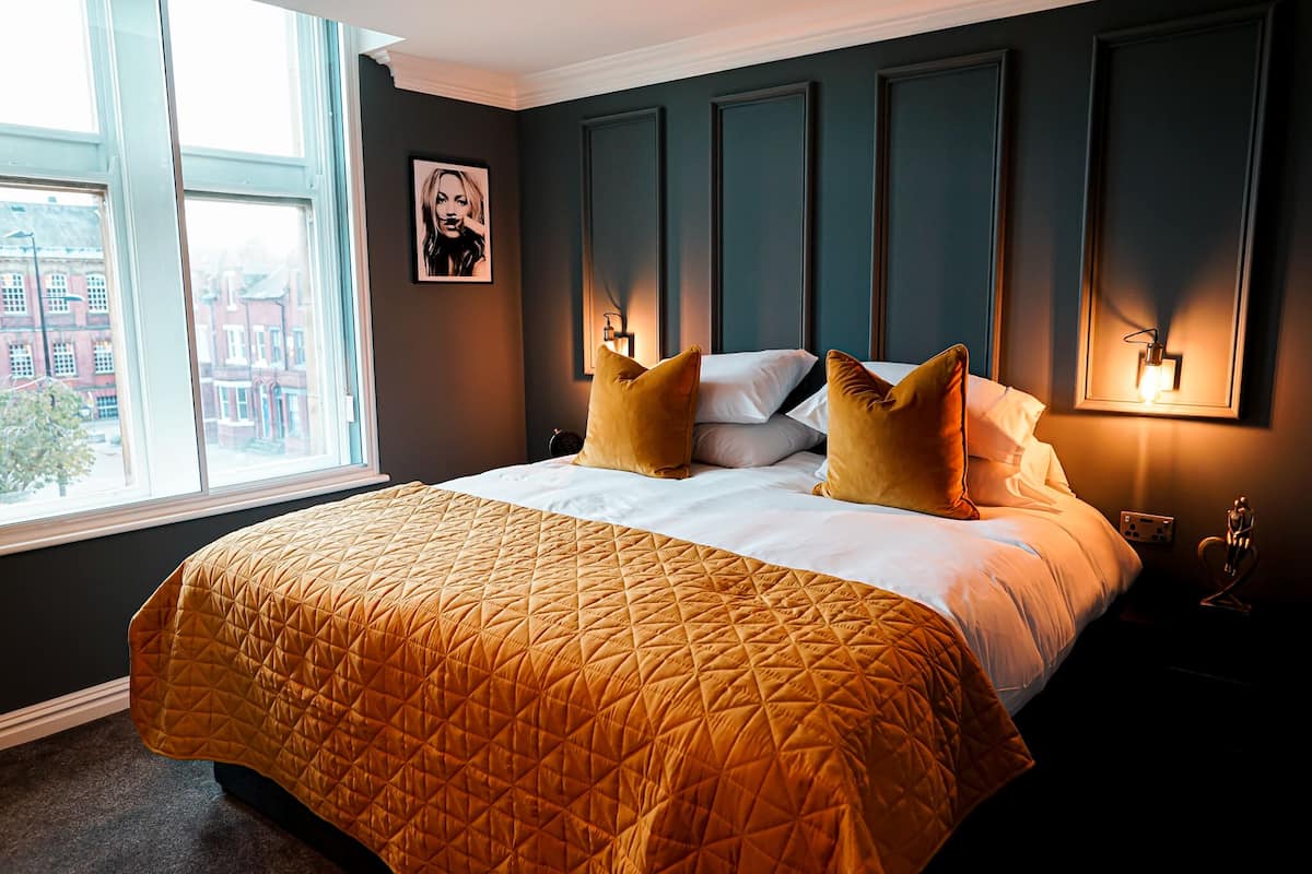 Une chambre d’hôtel avec un grand lit, une vue sur la ville par la fenêtre et un luminaire fixé au mur.