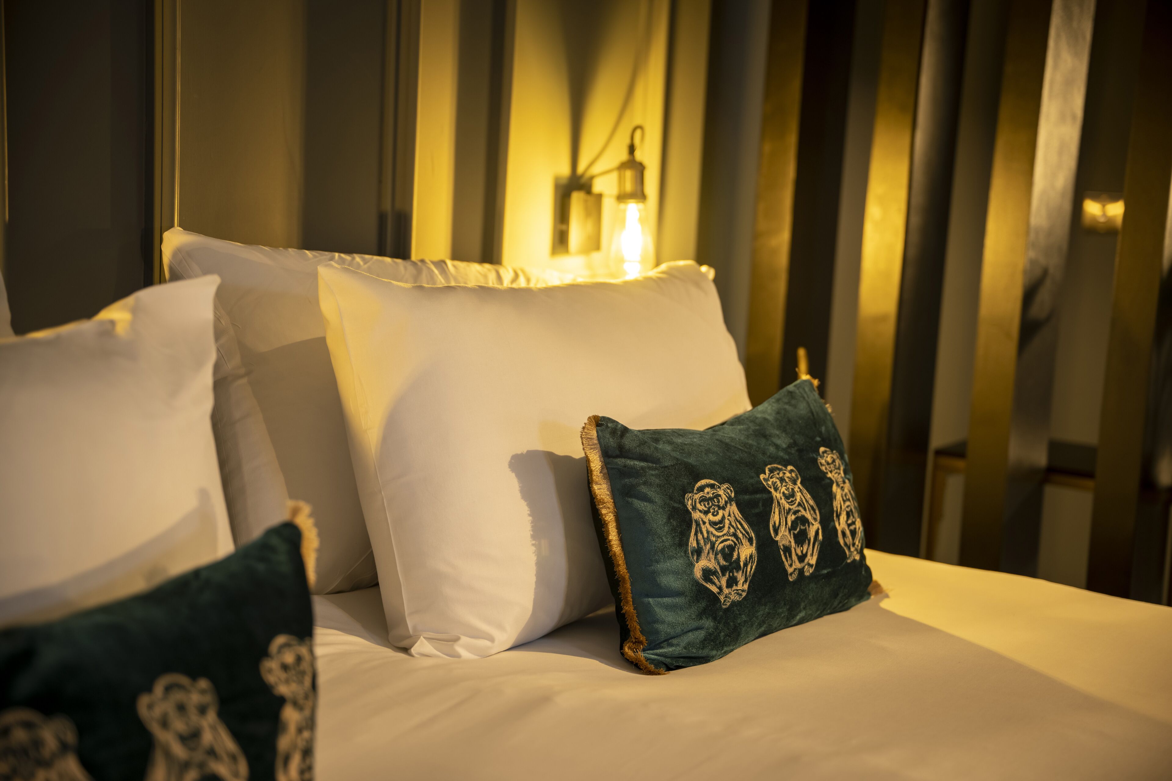 A neatly made bed with white linens and decorative pillows, including a green one with animal designs.