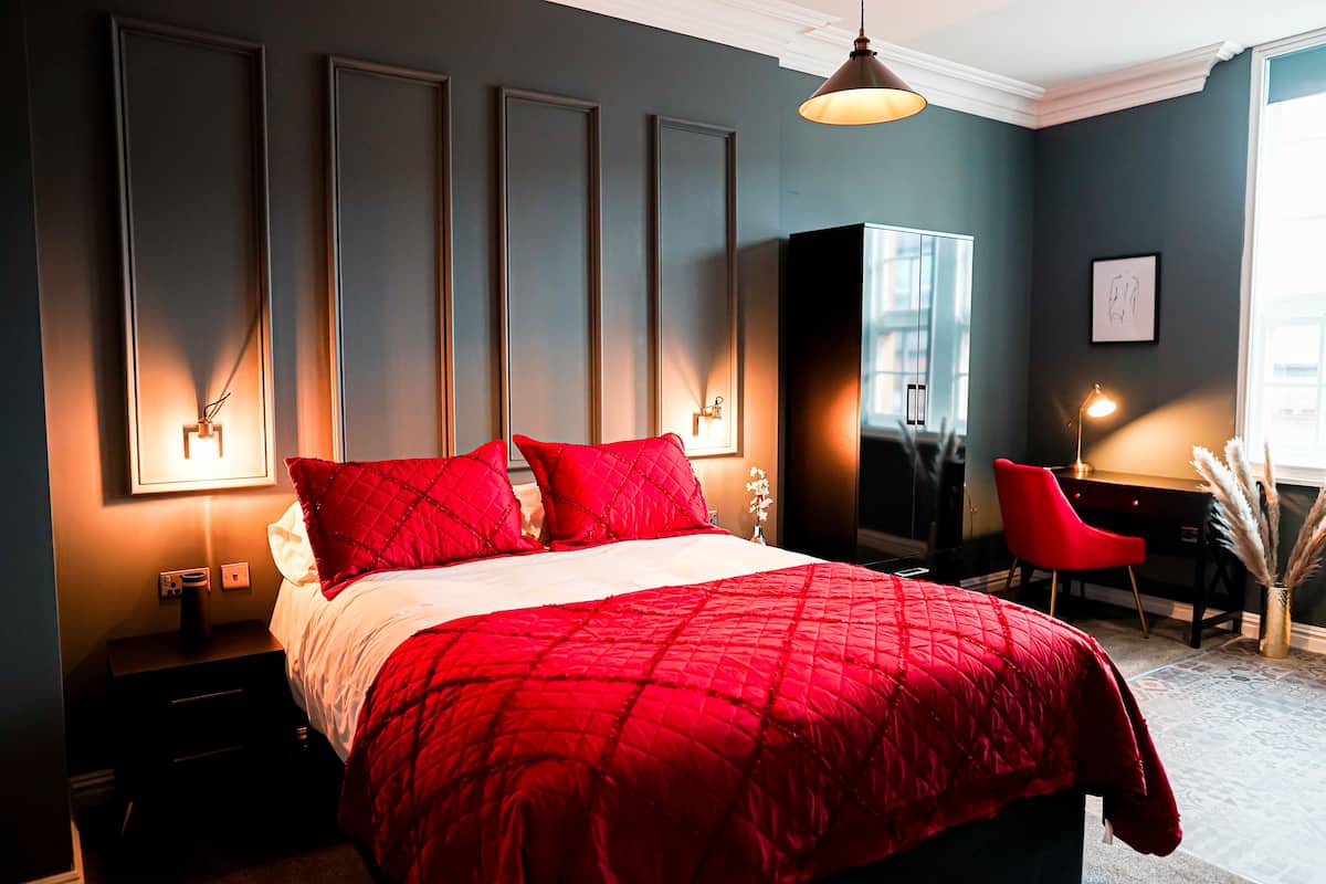 Une chambre à coucher avec un grand lit, une literie rouge, un bureau avec une chaise et une armoire.