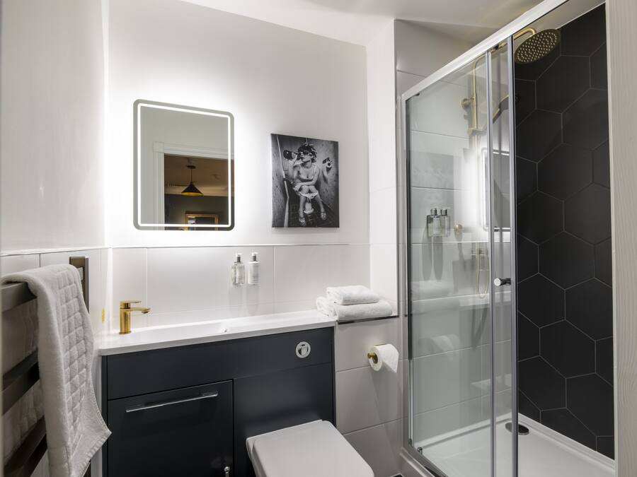 A modern bathroom with a glass-enclosed shower, a white sink with a gold faucet, and a black and white artwork above the mirror.