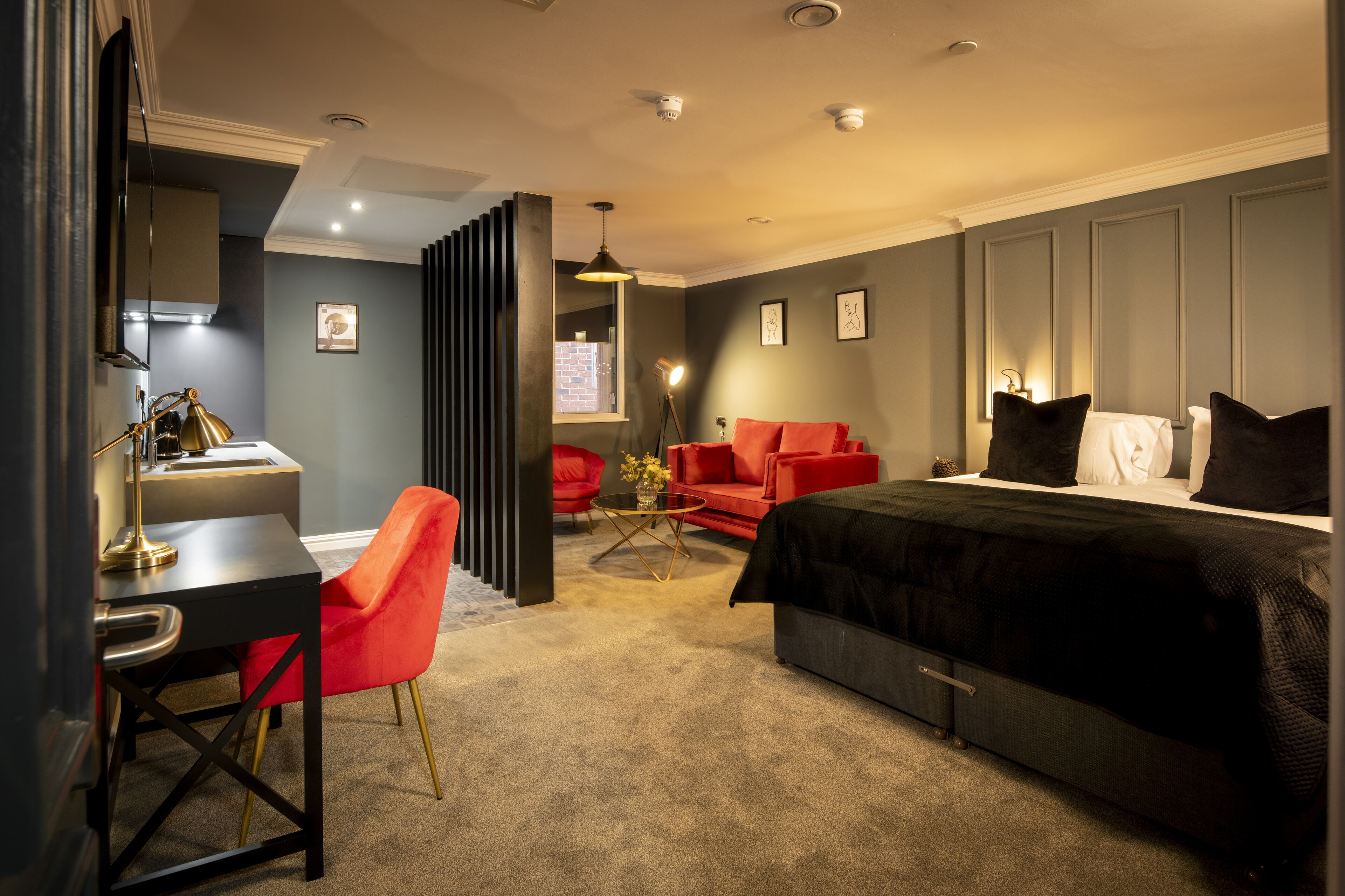 Habitación de hotel moderna con escritorio, silla roja y cama con ropa de cama negra.