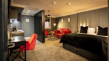 A modern hotel room with a desk, red chair, and a bed with black bedding.