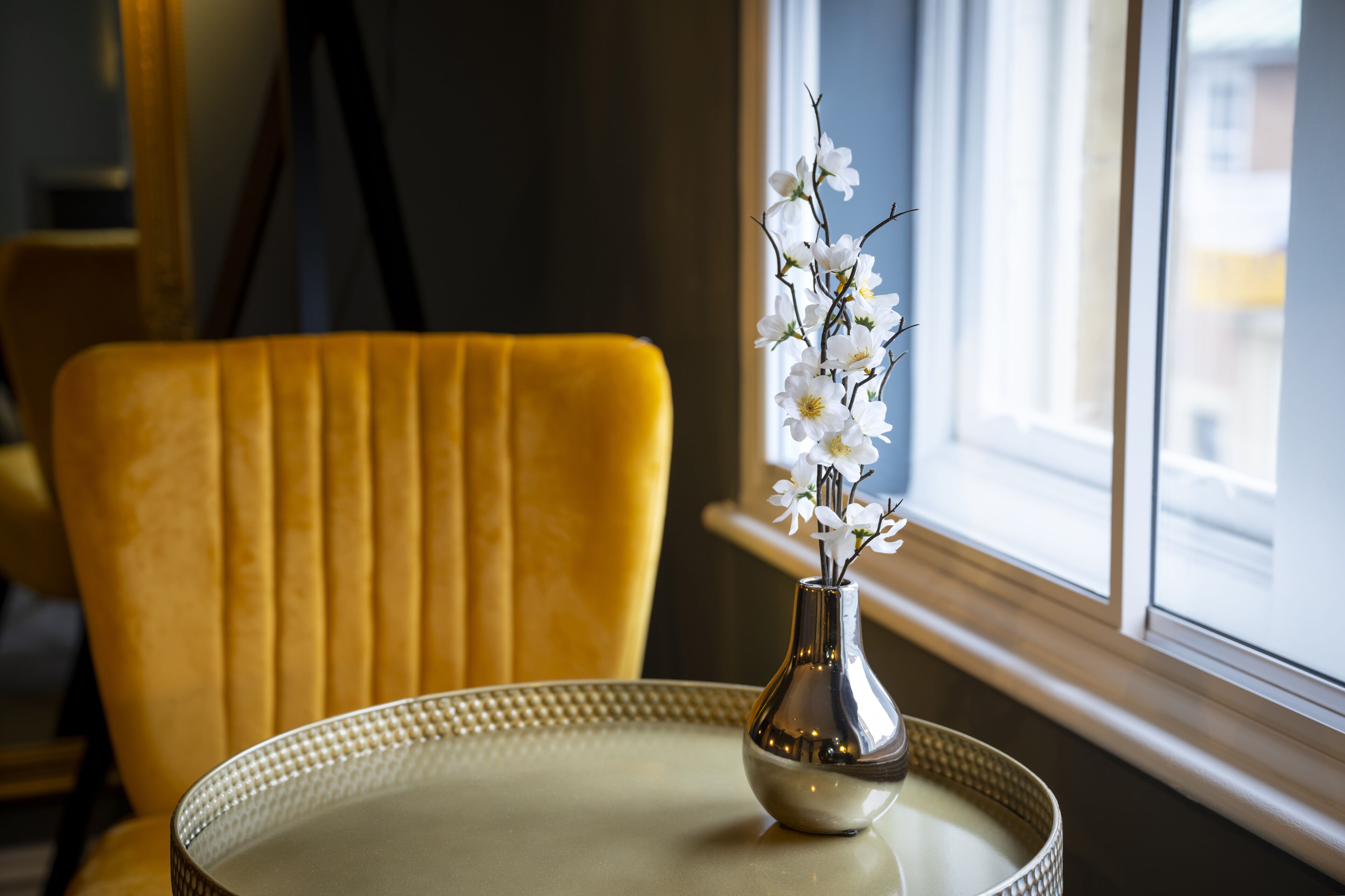 A yellow chair and a table with a vase of white flowers.