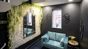 Ein dunkel gestalteter Raum mit einem hellblauen Sofa, einem Spiegel und einem kleinen runden Tisch mit Blumen in einer Vase.