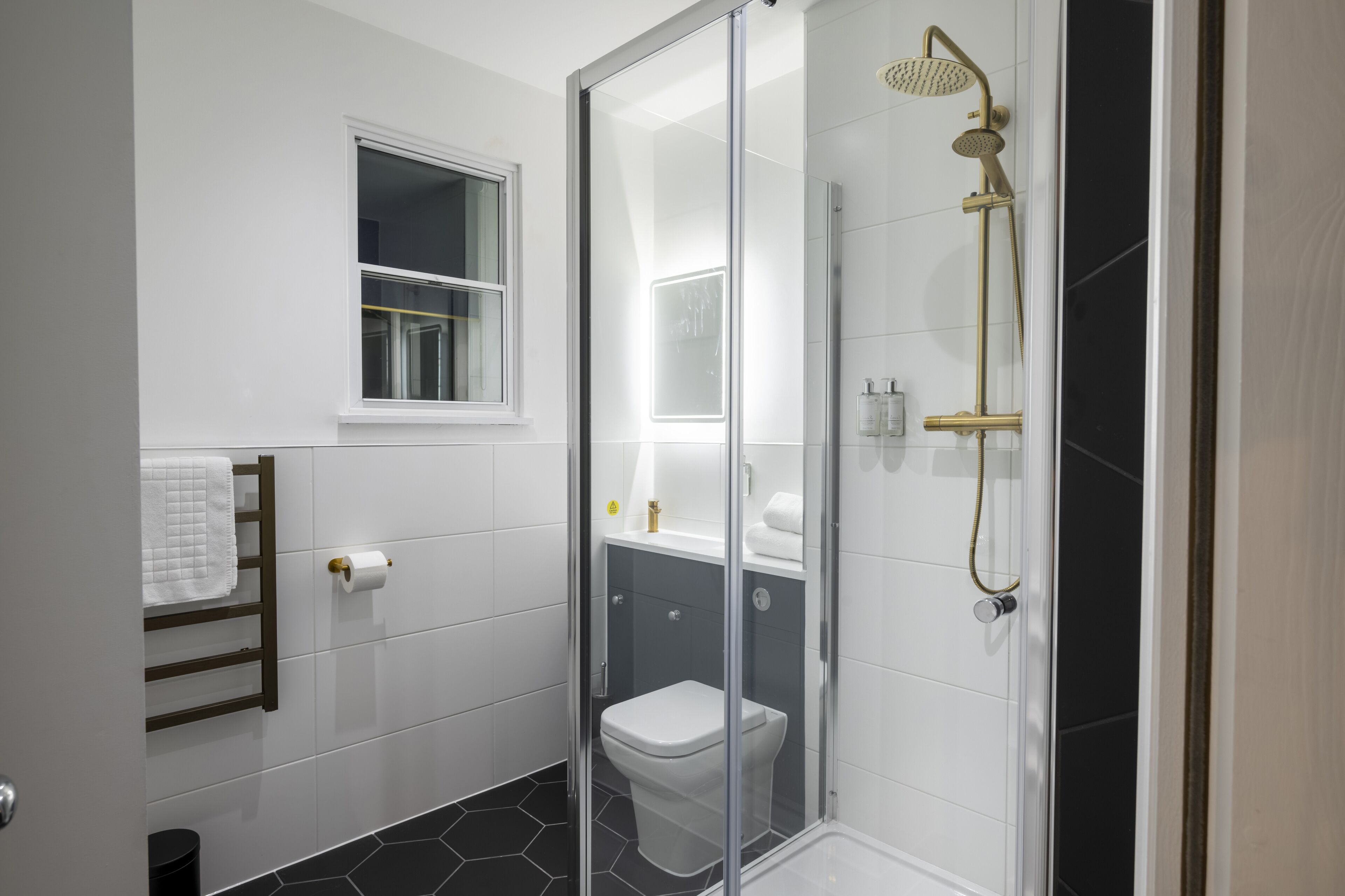 A modern bathroom with a glass shower enclosure, a toilet, and a towel rack.