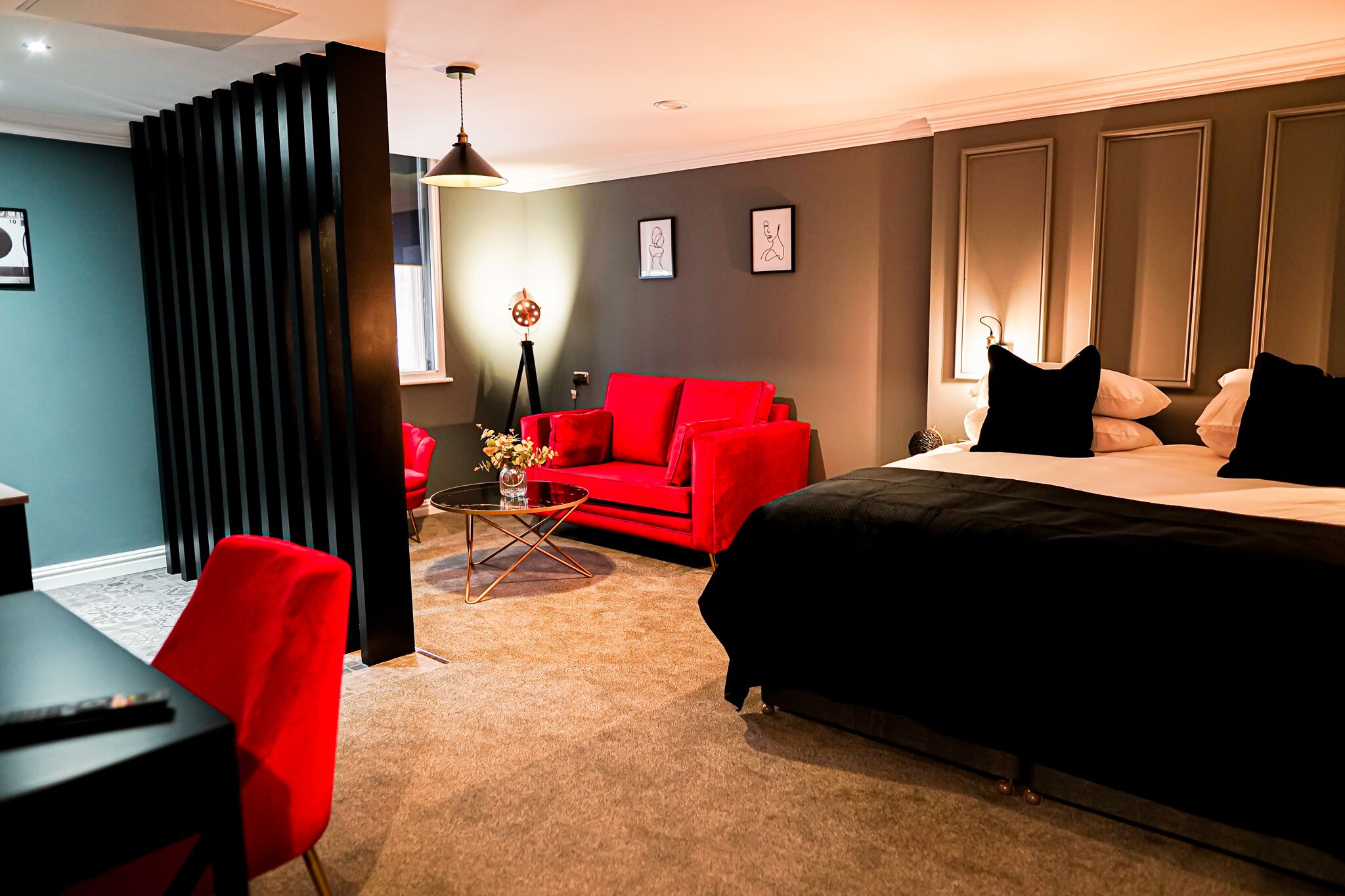 Una camera d'albergo moderna con un letto grande, un divano rosso, un tavolino da caffè e una scrivania con una sedia.