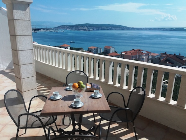Un balcon avec une table dressée pour deux personnes, offrant une vue sur la côte, avec des bâtiments et un pont.