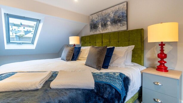 A bedroom with a large bed, two bedside tables, a window, and a painting on the wall. - Station Lodge By My Getaways (Brighton)
