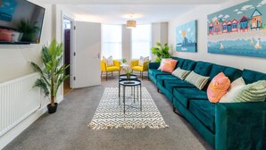 A living room with a teal sofa, yellow chairs, a TV, and artwork on the walls. - Station Lodge By My Getaways (Brighton)