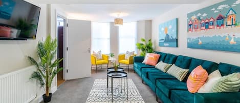 A living room with a teal sofa, yellow chairs, a TV, and artwork on the walls.