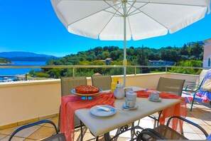 Een tafel gedekt met pizza, een koffiepot, kopjes en een schotel, op een balkon met uitzicht op een schilderachtig meer en heuvels.