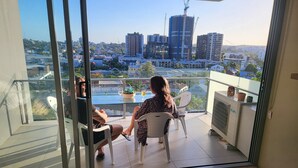 A balcony with a glass door, two chairs, a small table with a plant and a glass, and a potted plant on the railing. - Light apartment in amazing central location (South Brisbane)