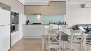 A modern kitchen with white cabinetry, a built-in oven, and a dining area with white chairs and a table. - Light apartment in amazing central location (South Brisbane)