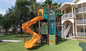 Playground and residential building with a symmetrical design and landscaped surroundings.