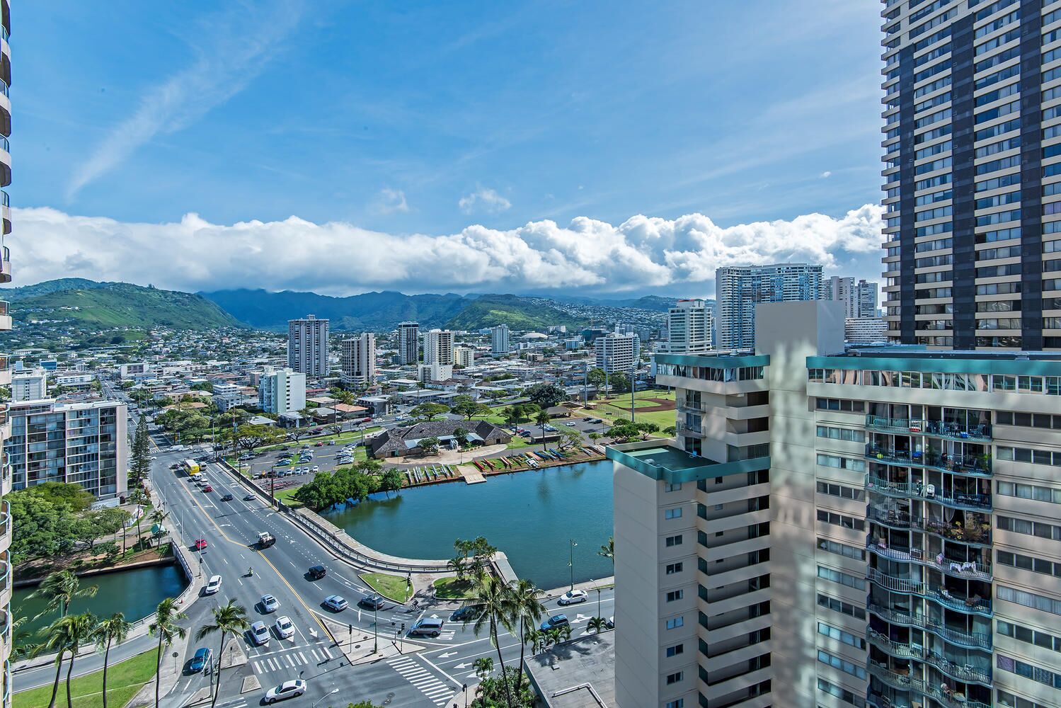 A cityscape with modern high-rise buildings, a marina, and a road leading to a roundabout.