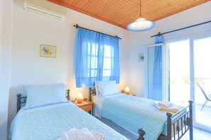 A room with two beds, a ceiling fan, a window with blue curtains, and a door leading to a balcony.
